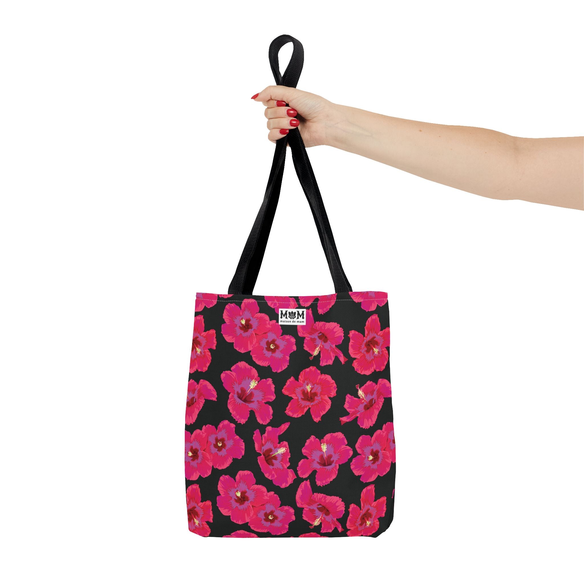 Black tote bag with pink floral pattern on black background, held by a hand.