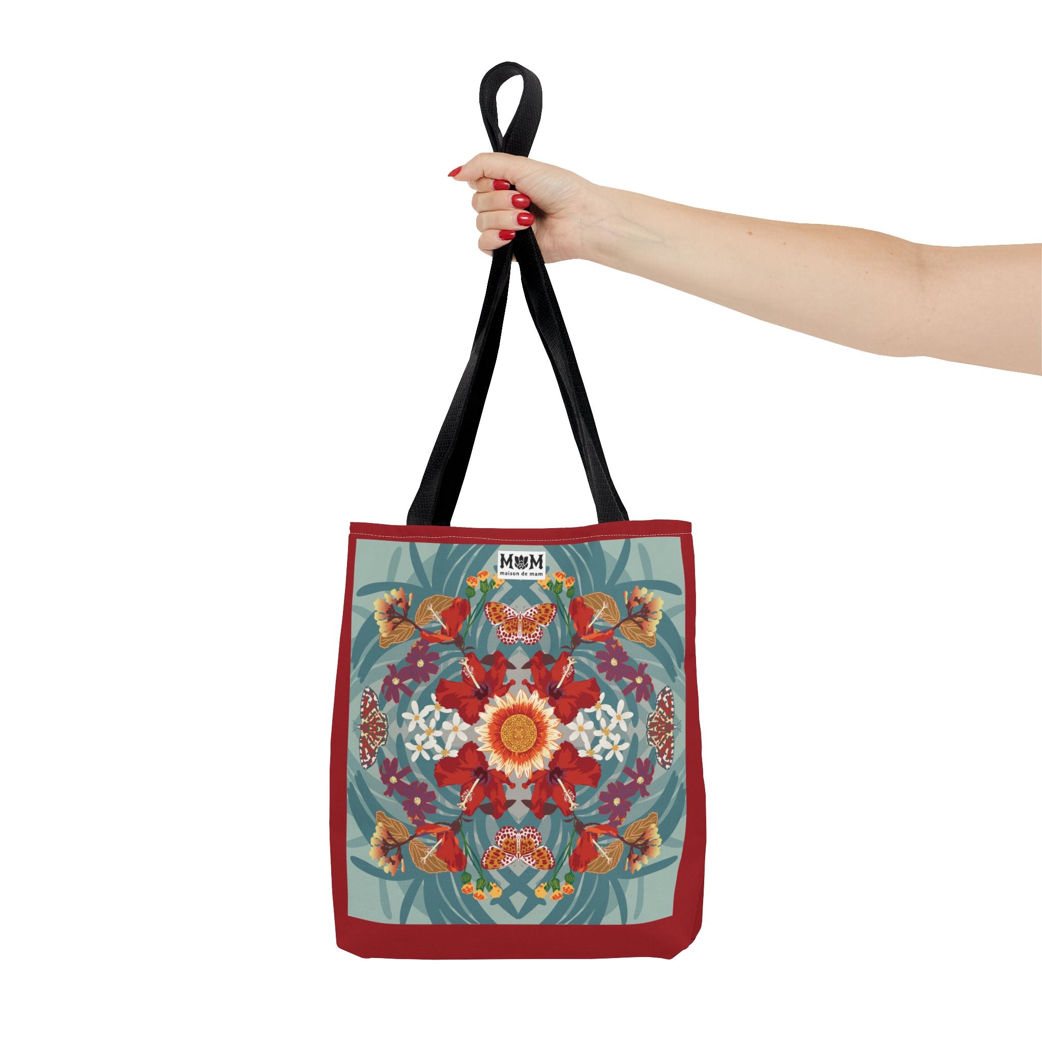Red and muted teal tote bag with floral design held by a hand on a white background
