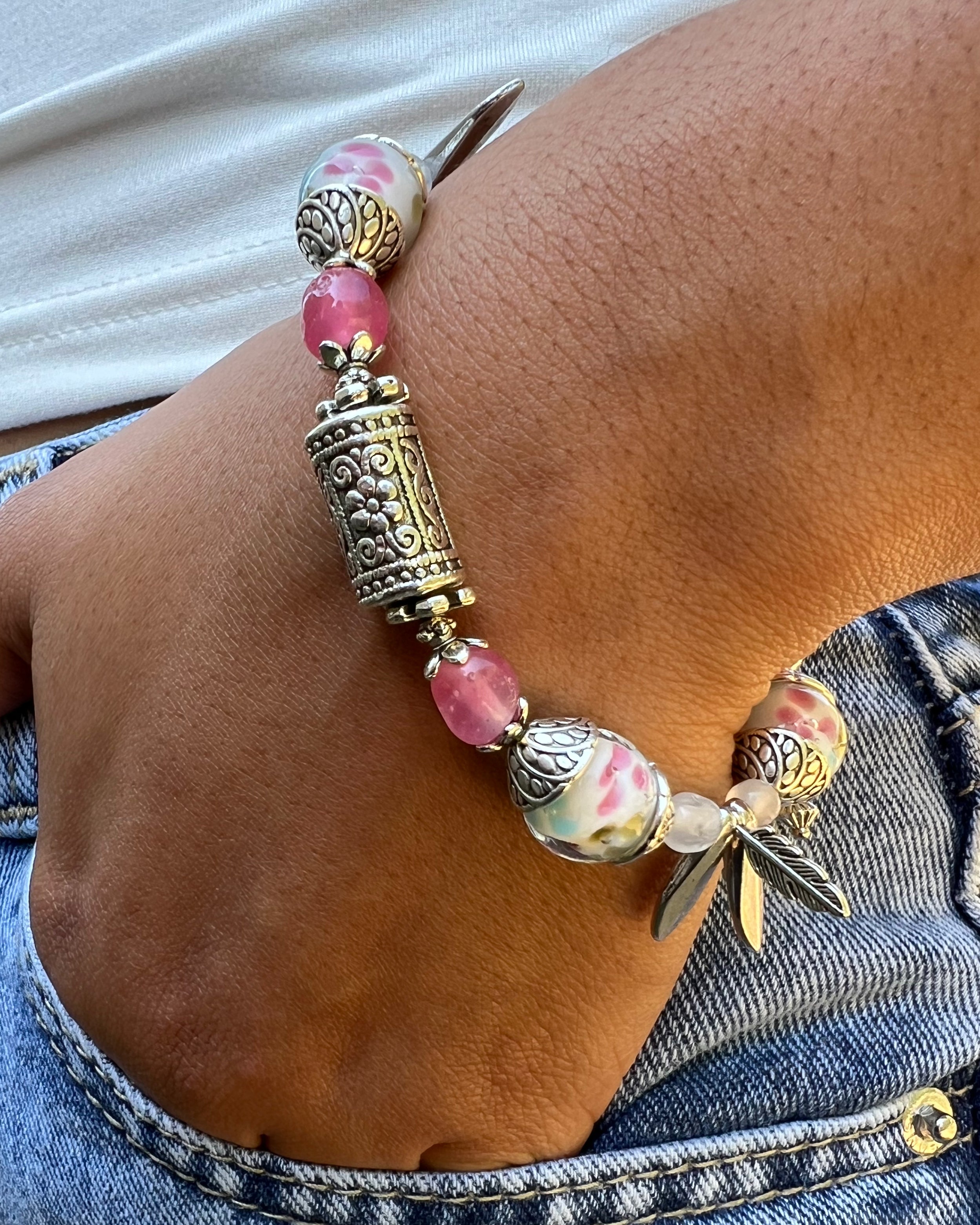 Bracelet with pink beads and gold accents on a wrist, wearing denim jeans.