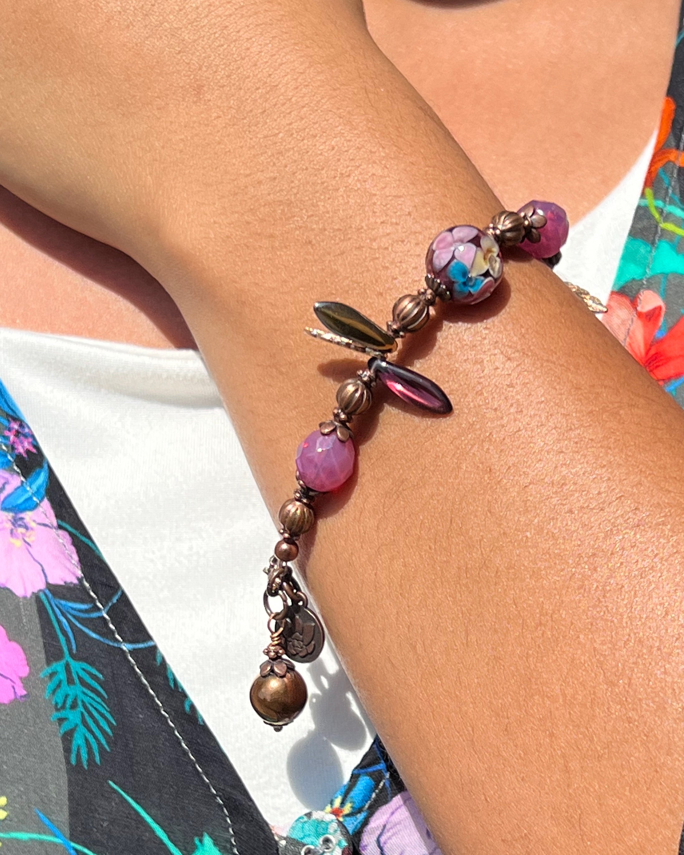 Close-up of a beaded bracelet on a person's wrist with a floral-patterned garment.